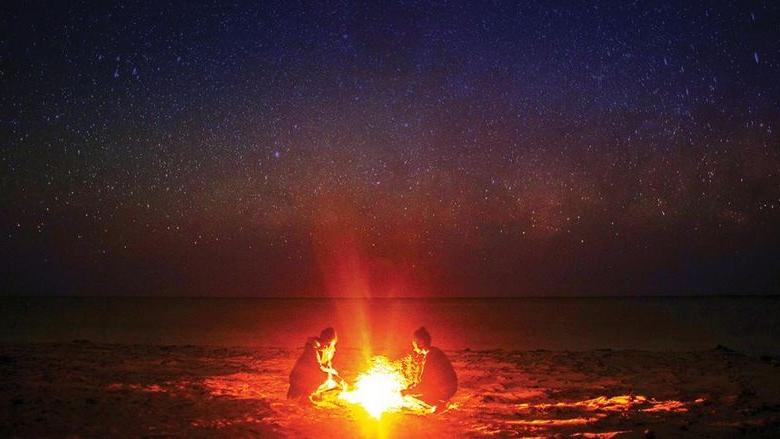 Two individuals sitting around a campfire beneath a star-mottled sky